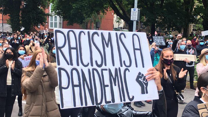 A crowd holding up a banner that says racism is a pandemic