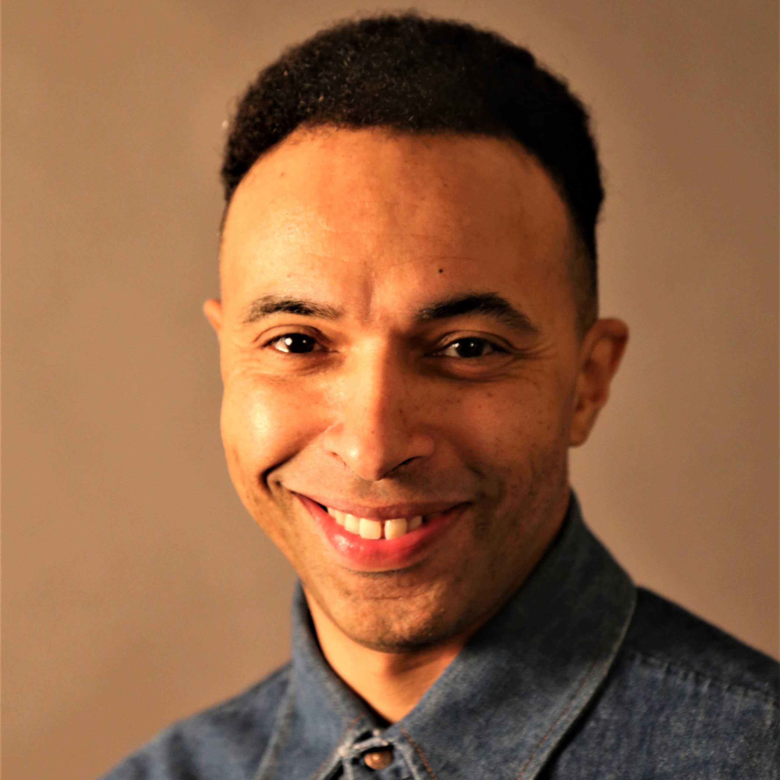 Kwesi Johnson. A headshot of a smiling man with light brown skin and short dark hair.