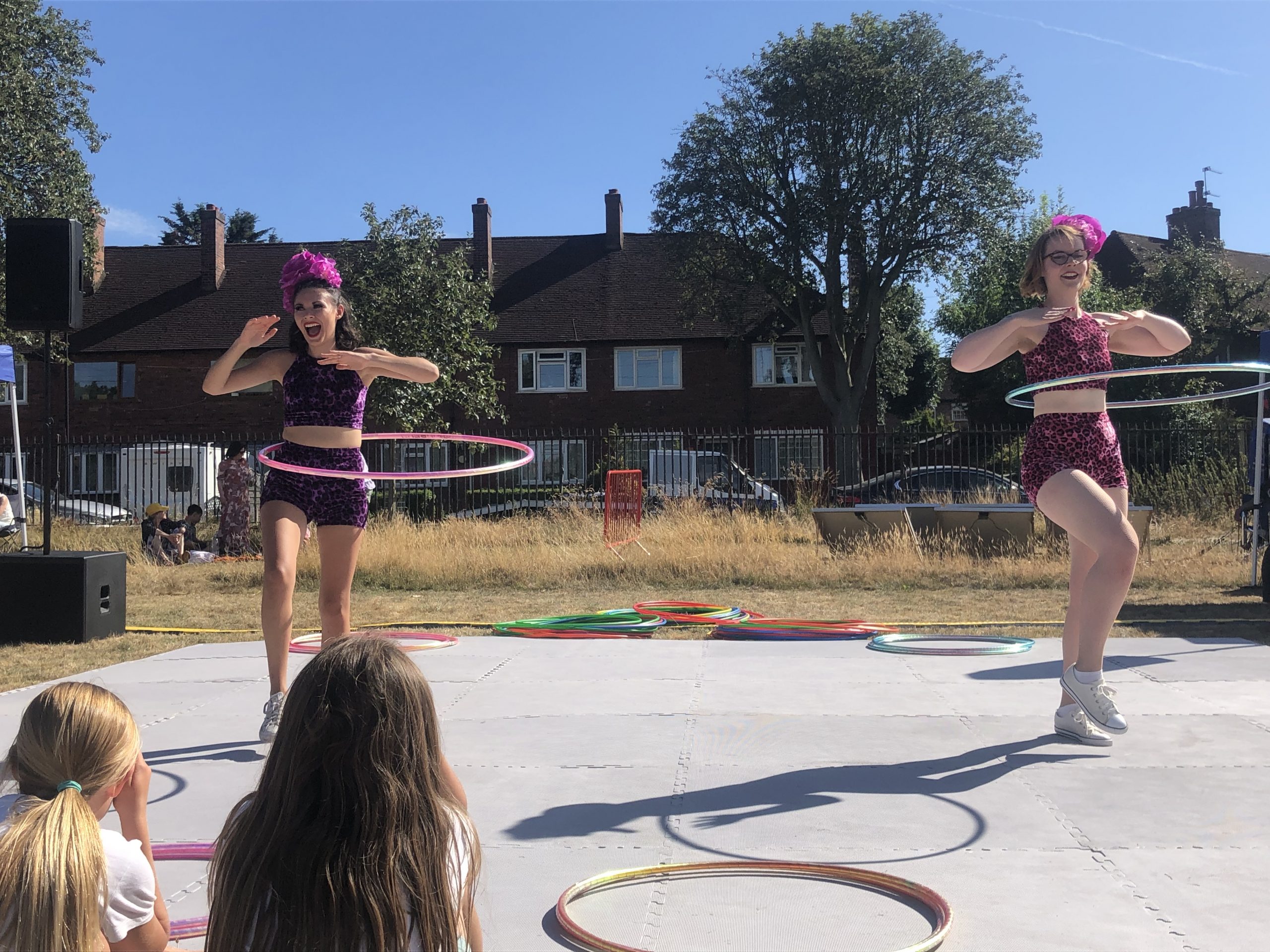 Queenscroft Park Picnic Creators Group. Two women pose on an outdoor stage with hula hoops swinging around their middles