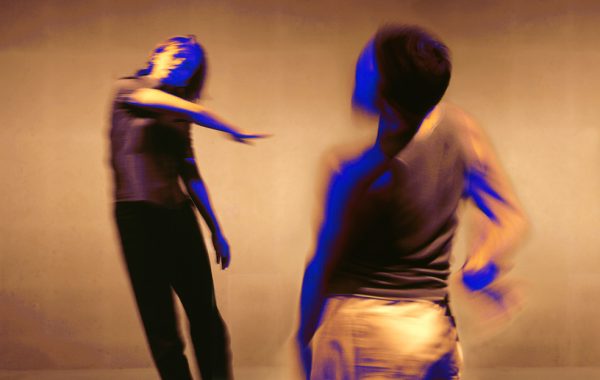 30 years in pictures: Physical Recall and Akram Khan. Two dancers are blurry from movement. One leans back away from the other whose arm is thrown across her body.
