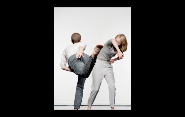 30 years in pictures: Compass Commissions Part 2. Two dancers move in front of a white background. One is turned away, their leg flicking out behind them. The other bends to the left, their right arm covering their face