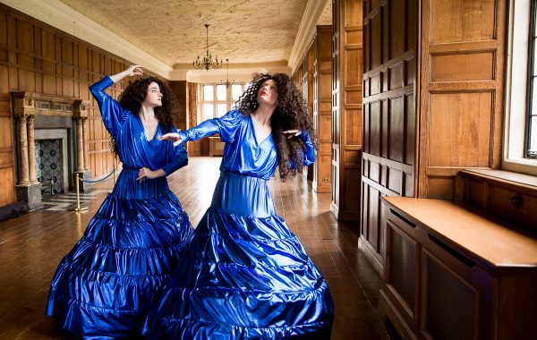 30 years in pictures: GLORIA! and Charlton House. Two dancers in bright blue hooped dresses pose in the long gallery, a wood panelled room at Charlton House.
