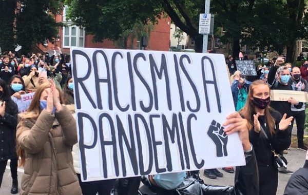 30 years in pictures: Creating through a Crisis. A group hold up a banner which reads: racism is a pandemic.